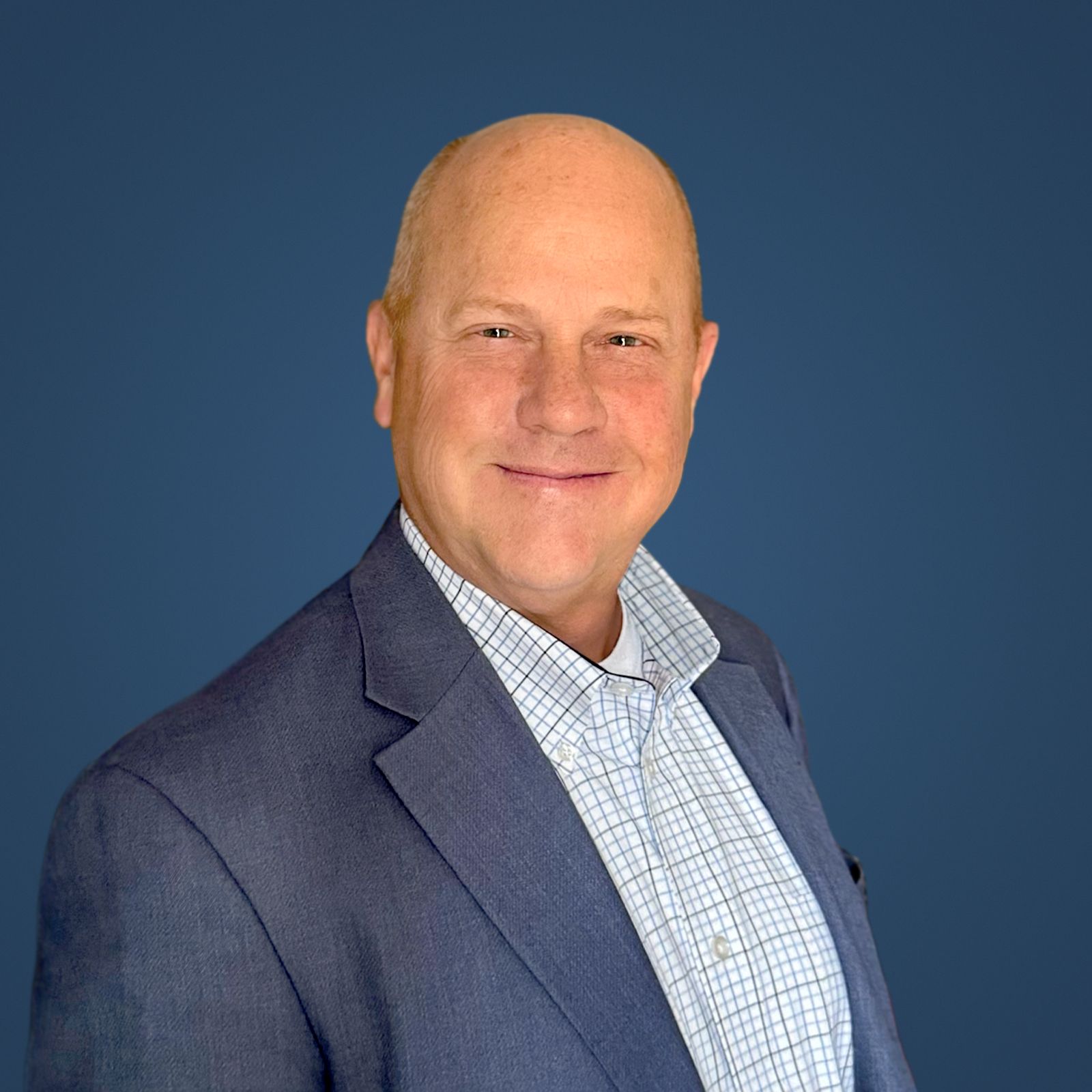 A bald man in a suit and plaid shirt is smiling for the camera.