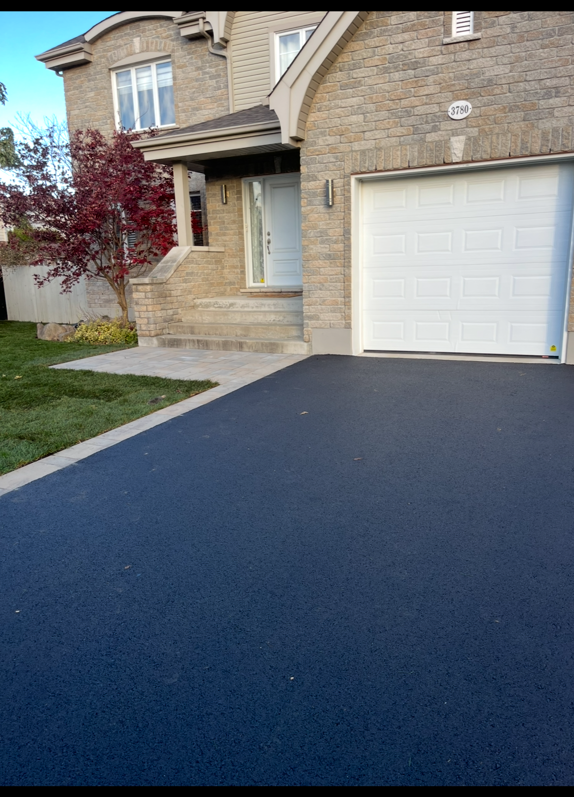 Une maison avec une allée noire et une porte de garage blanche.