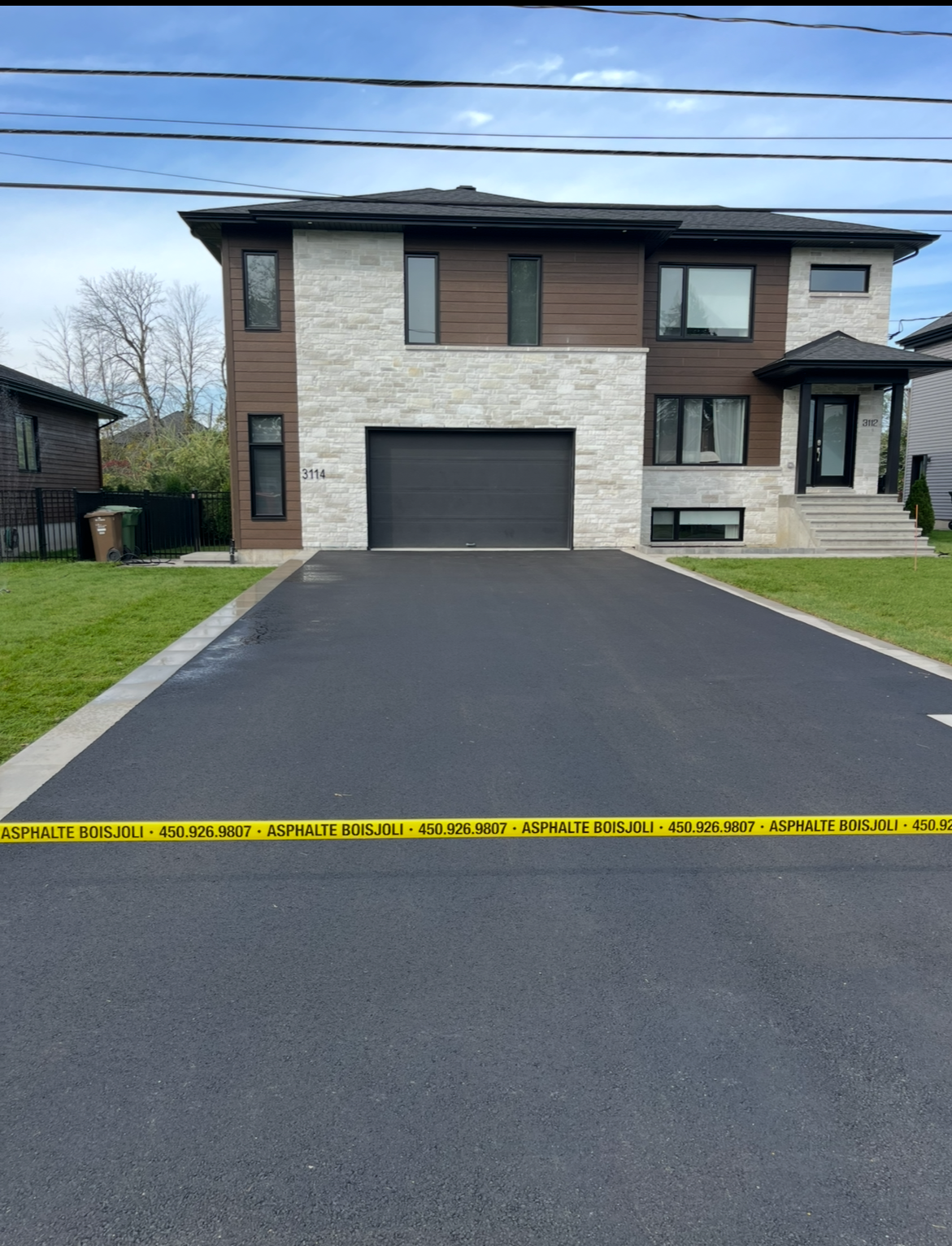 Une grande maison avec une porte de garage noire est entourée de ruban de prudence
