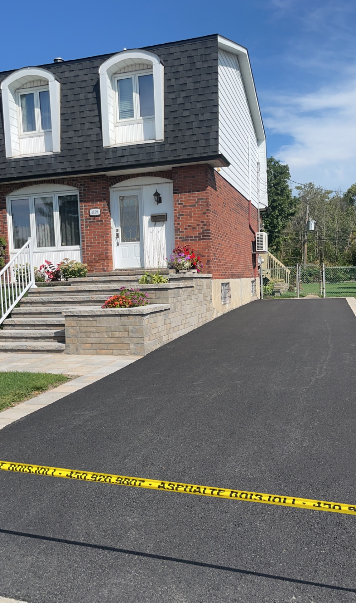 Une maison en briques avec un toit noir et une allée noire devant.