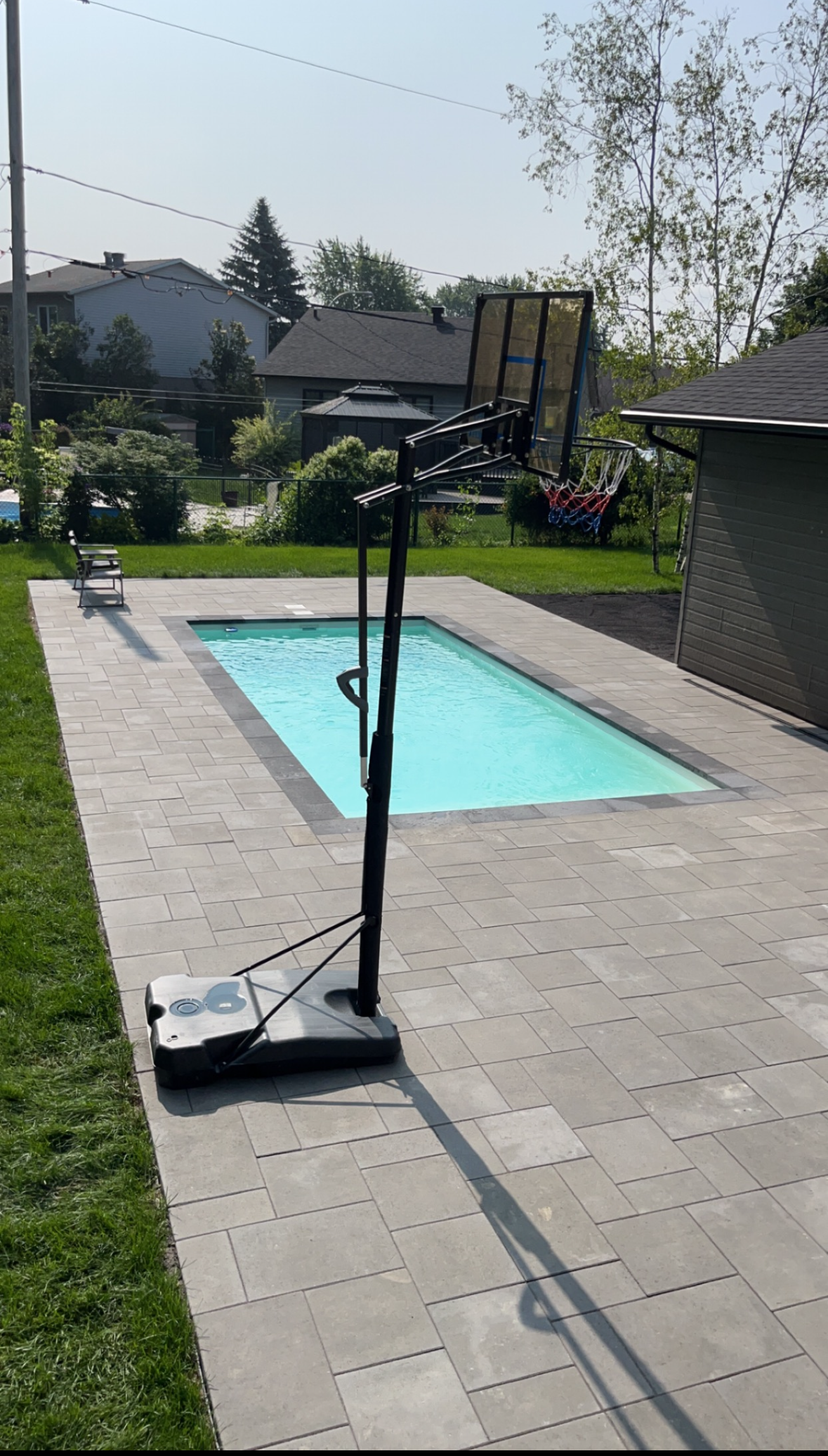Un panier de basket est assis à côté d'une piscine dans un jardin.