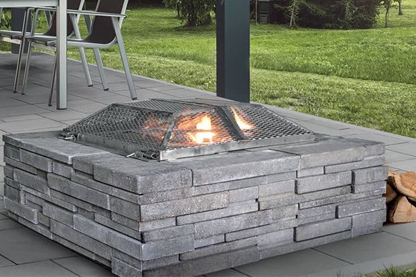 Un foyer est installé sur une terrasse à côté d'un tas de bûches.