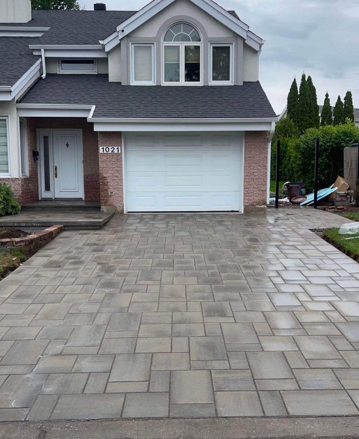 Une maison en briques avec une porte de garage blanche et une allée en briques devant.