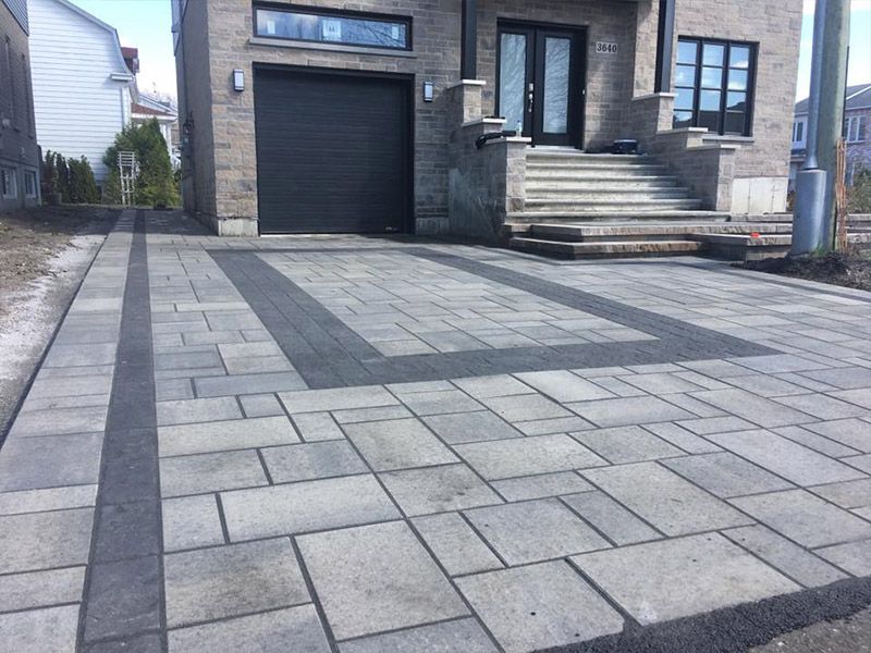 Une allée devant une maison avec une porte de garage noire.