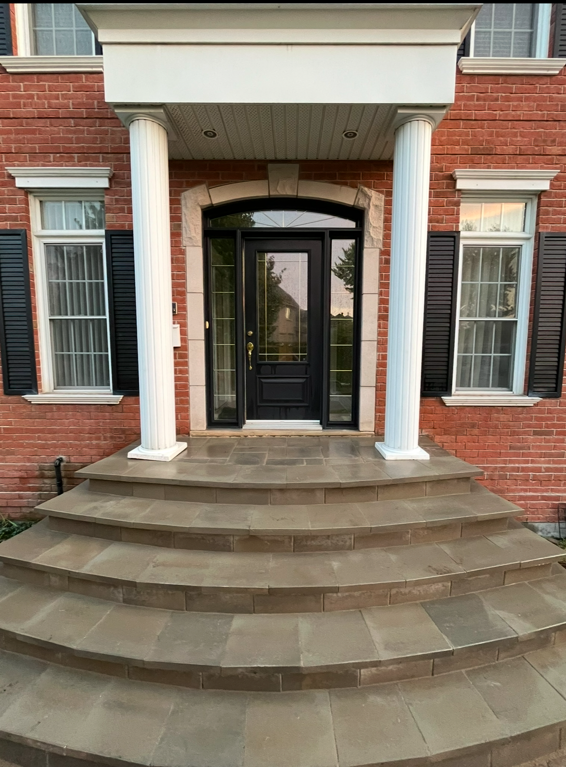 Une maison en briques avec une porte noire et des marches qui y mènent.