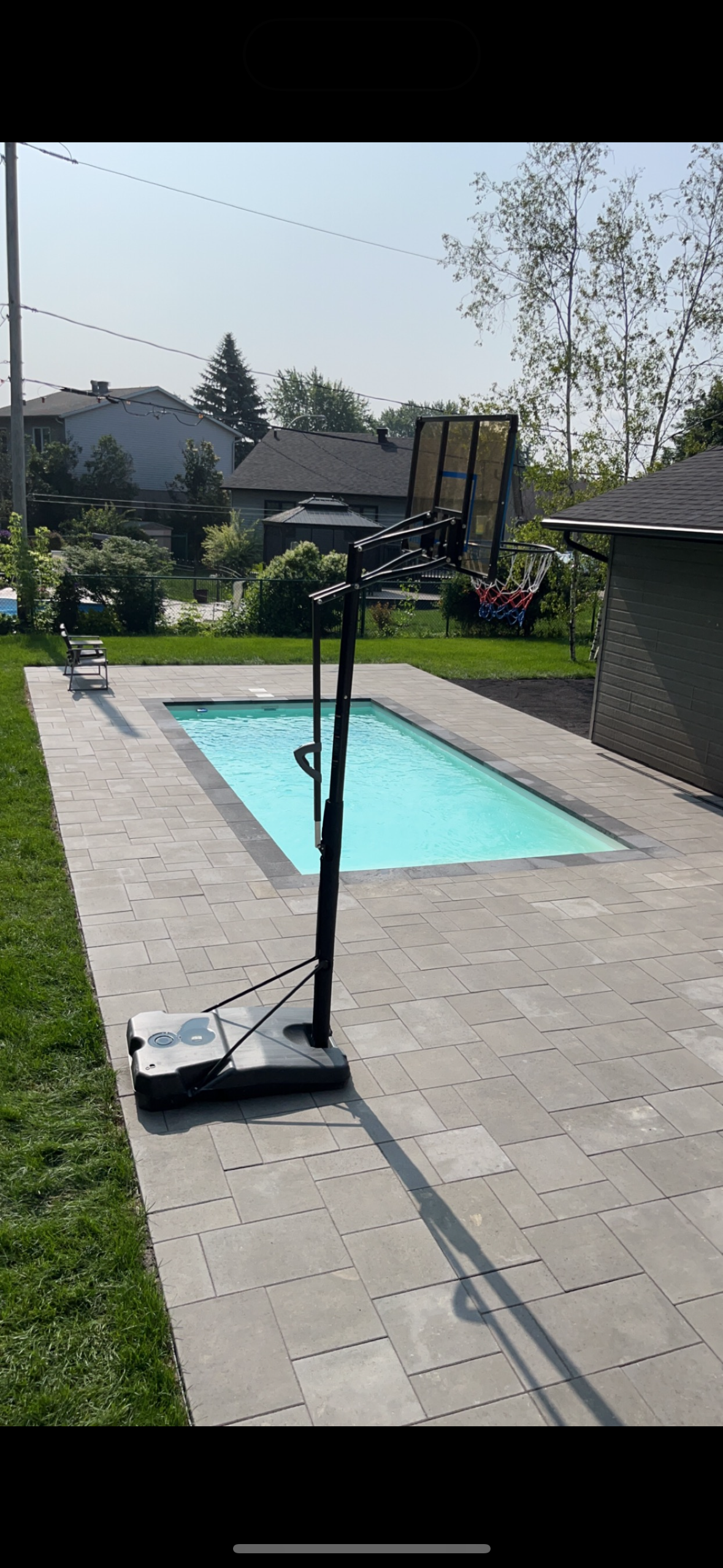 Un panier de basket est assis à côté d'une piscine dans un jardin.