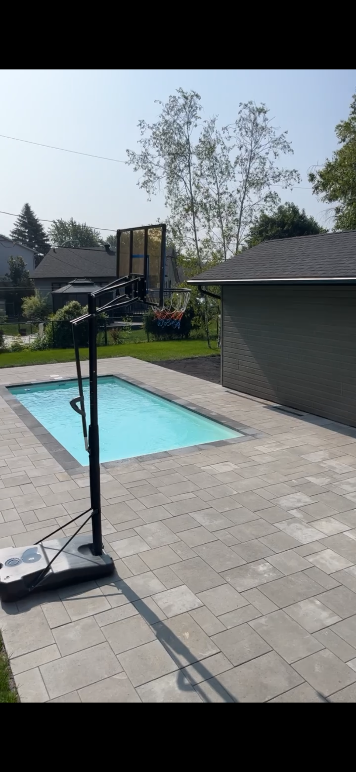 Un panier de basket est assis à côté d'une piscine dans une cour arrière.
