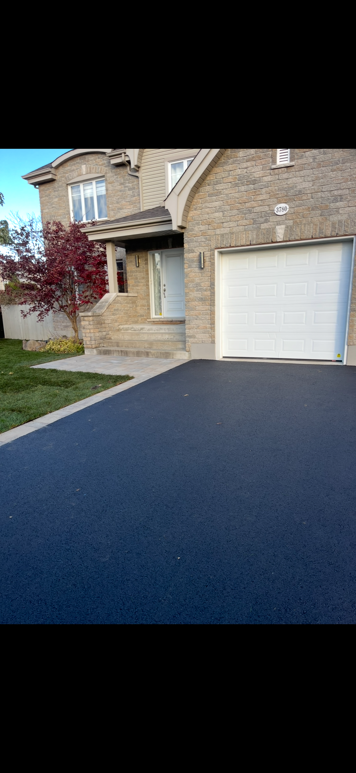 Une maison avec une allée noire et une porte de garage blanche.