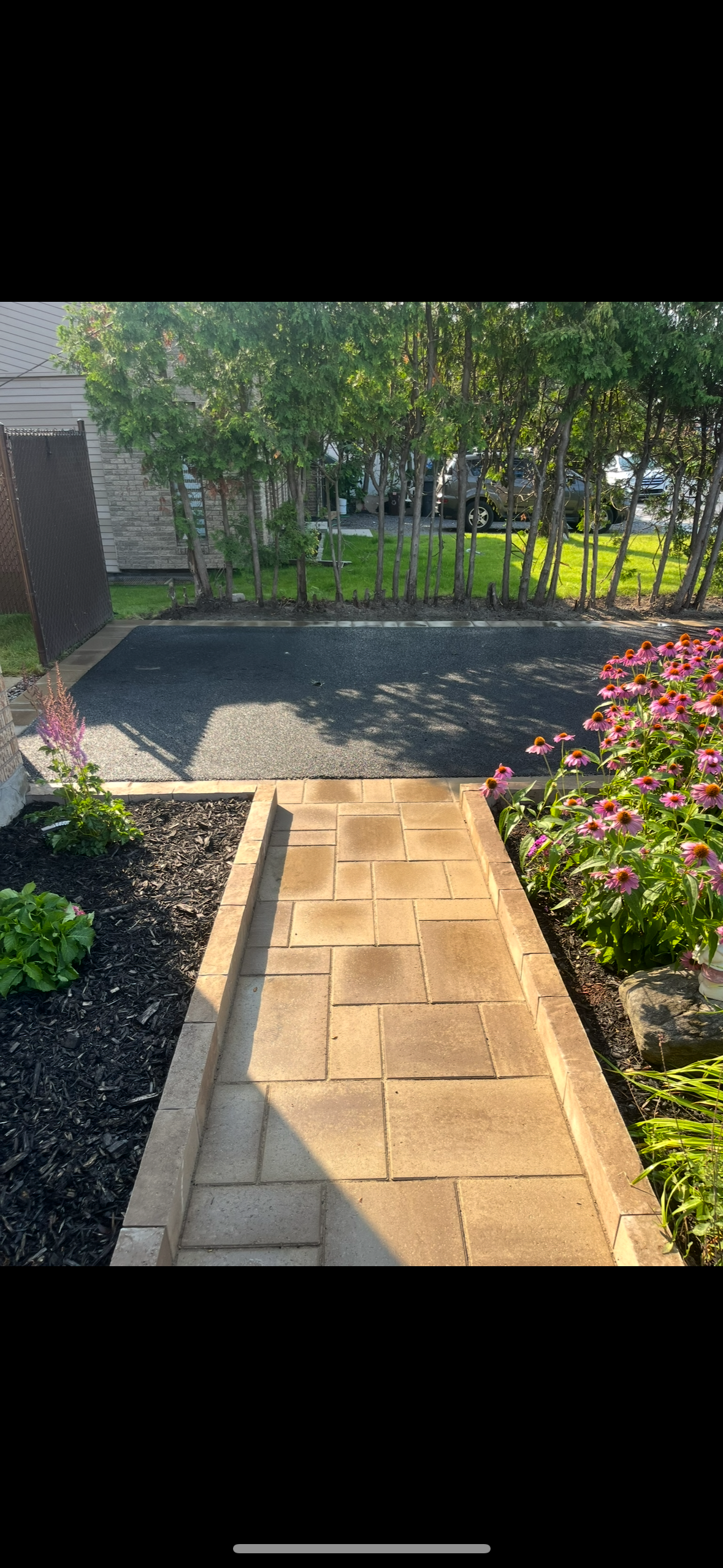 Une allée en briques menant à un jardin avec des fleurs et des arbres.