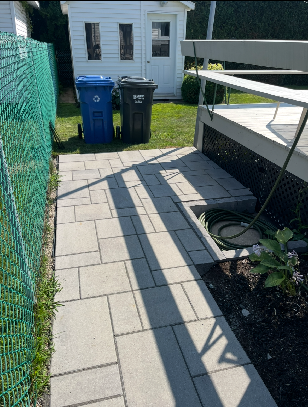 Deux poubelles sont posées sur un trottoir à côté d'une clôture.