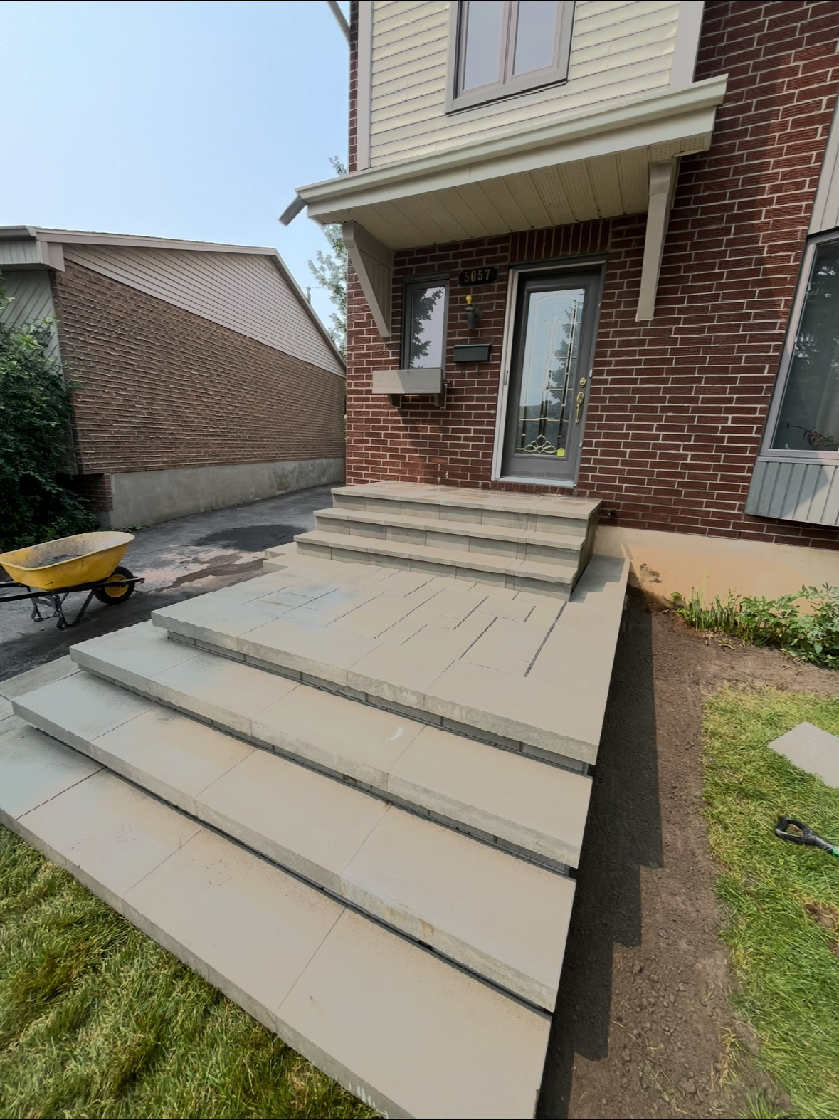 Une brouette est garée devant une maison en briques.