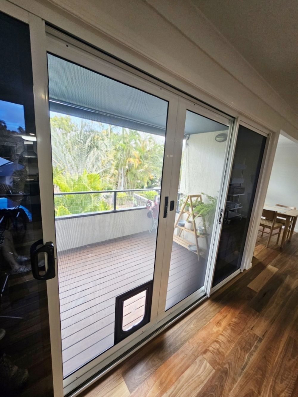 A Sliding Glass Door With A Cat Door In A Living Room Leading To A Balcony — Modern Window Furnishings In Gin Gin, QLD