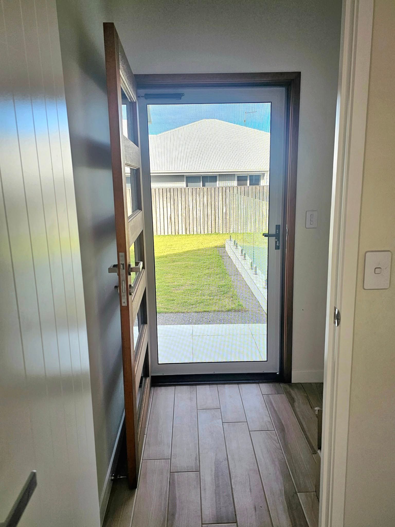 A Wooden Door With A Screen On It Is On A White Brick Wall — Modern Window Furnishings In South Kolan, QLD
