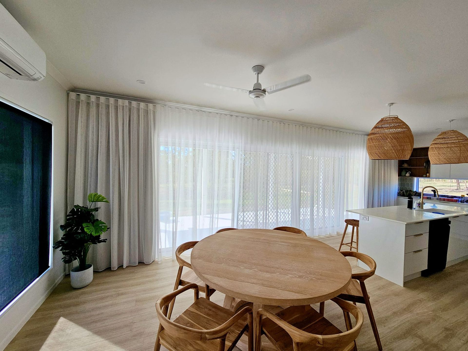 Sheer beige curtains hang in front of a window, with a white wall and trim visible. Sunlight filters through the curtains. — Modern Window Furnishings In Agnes Water, QLD