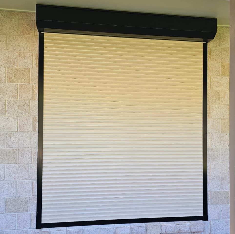 A White Roller Shutter On A Window With A Black Frame On A Brick Wall — Modern Window Furnishings In Childers, QLD