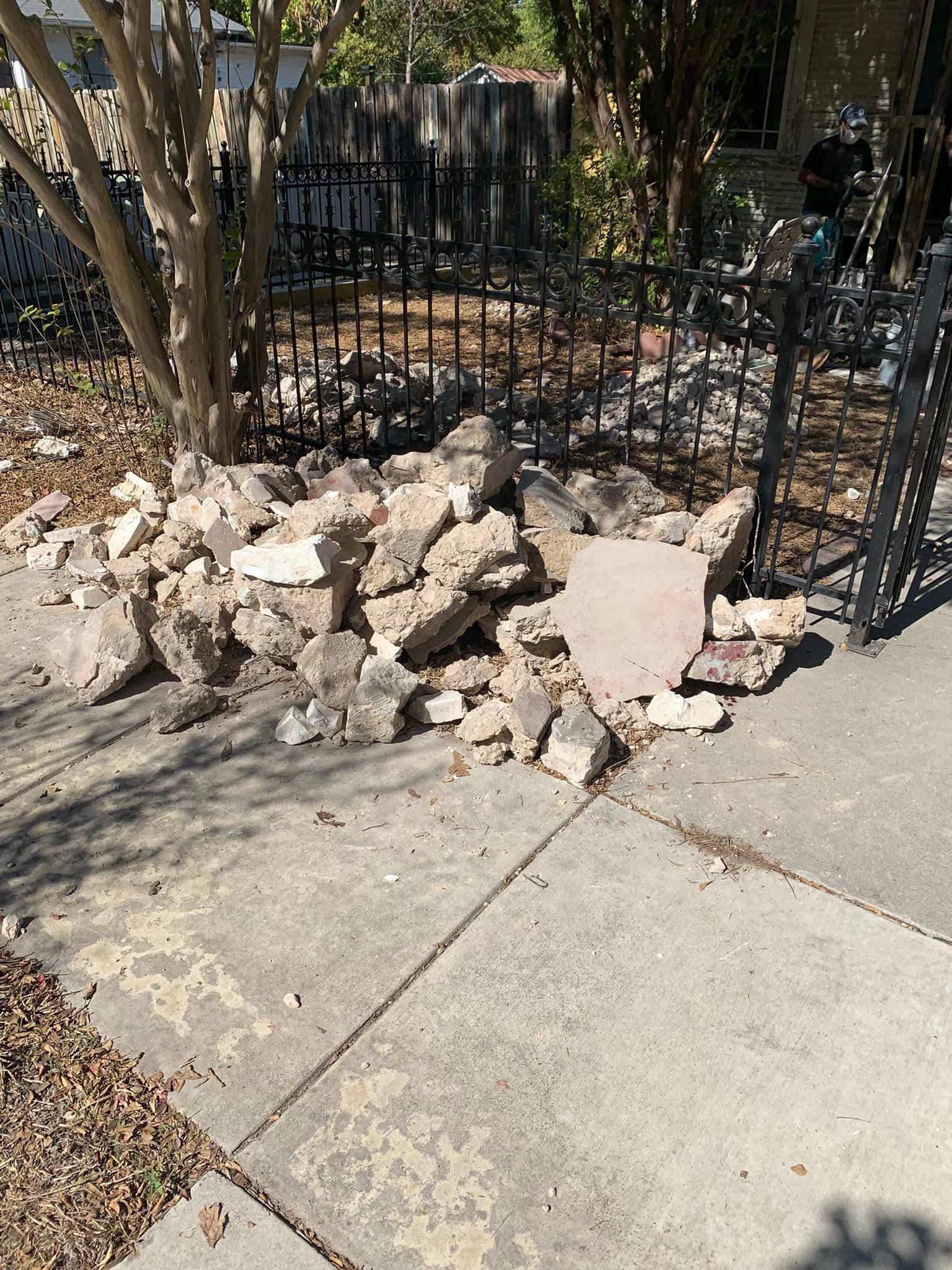 A pile of rocks is sitting on the sidewalk next to a fence.