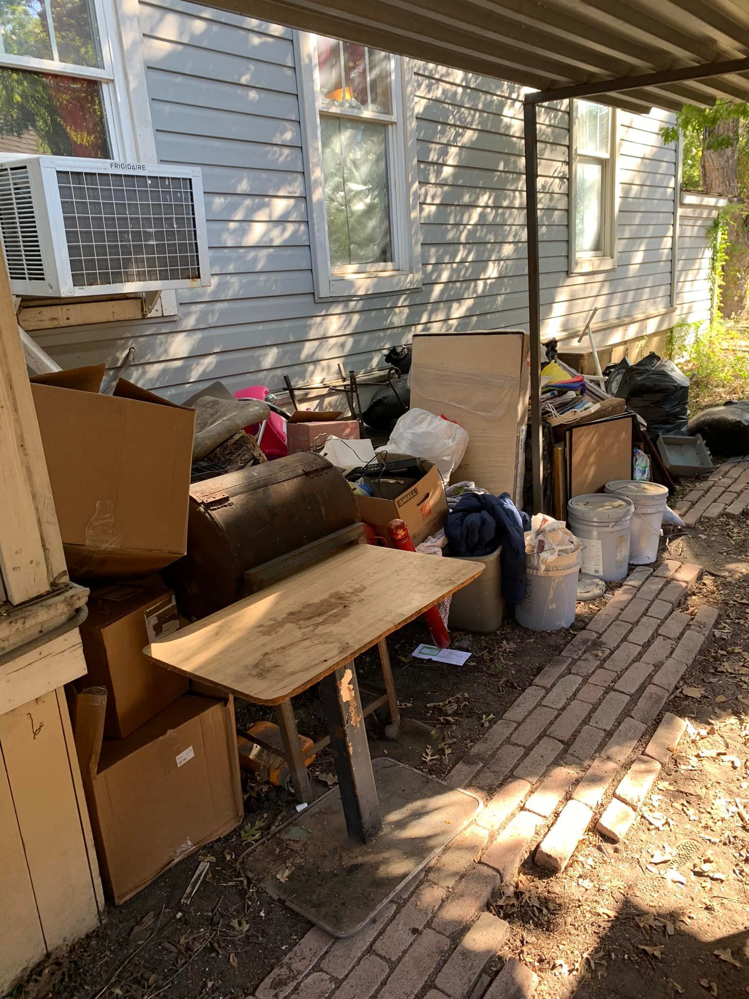 Pile of clutter and boxes against a weathered building under a metal overhang.