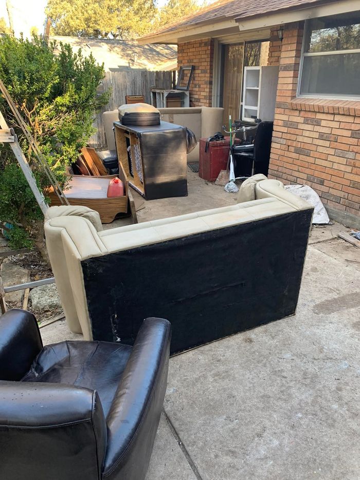 A bunch of furniture is sitting on the ground in front of a house.