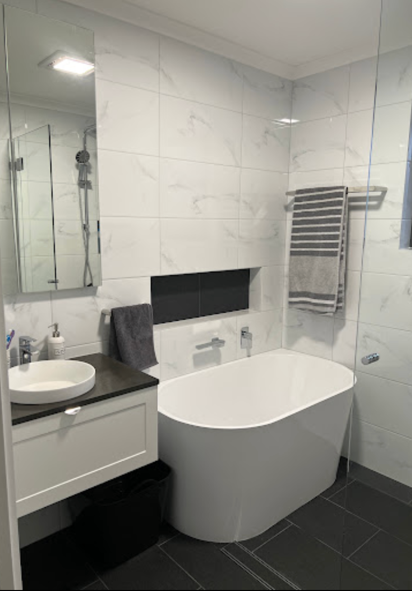 A bathroom with a bathtub , sink , mirror and towel rack.