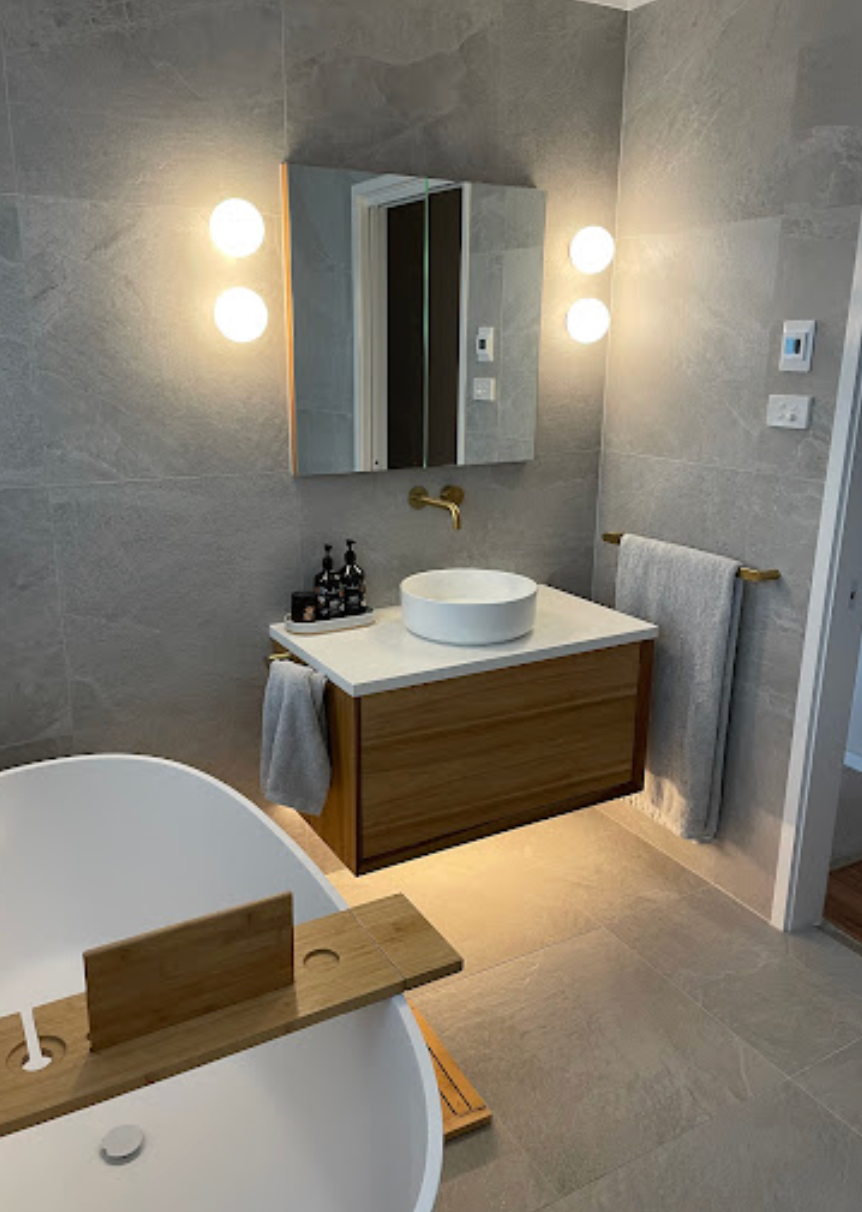 A bathroom with a bathtub , wooden detailed sink and mirror.