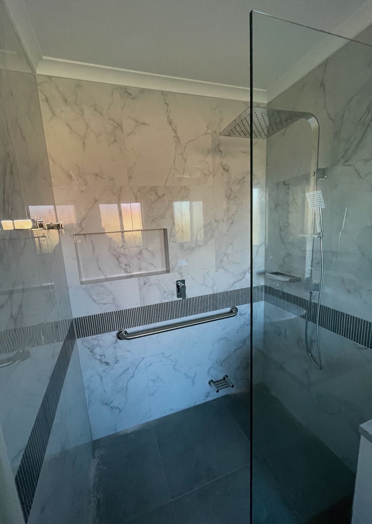 A bathroom with marble walls and a walk in shower with a glass door.