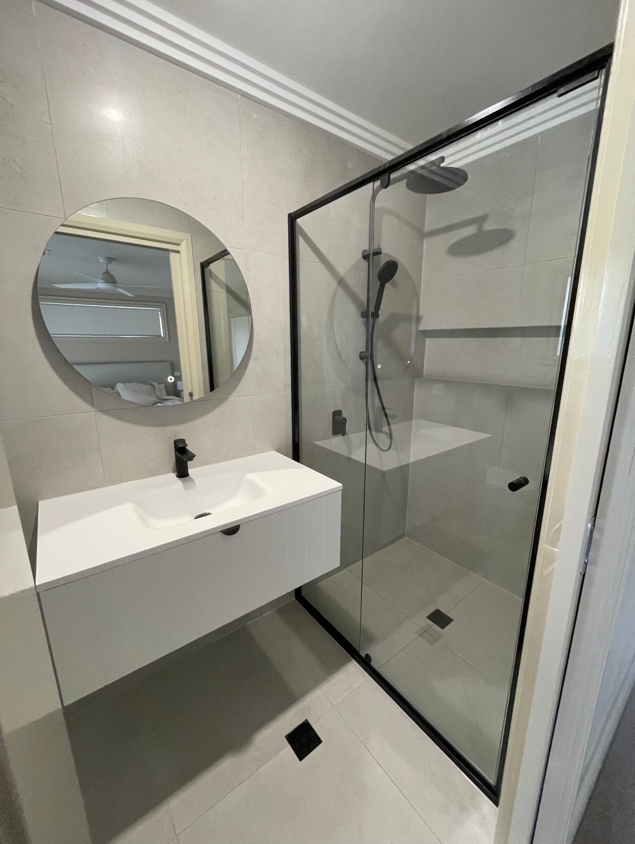 A bathroom with a sink and a shower with a round mirror.