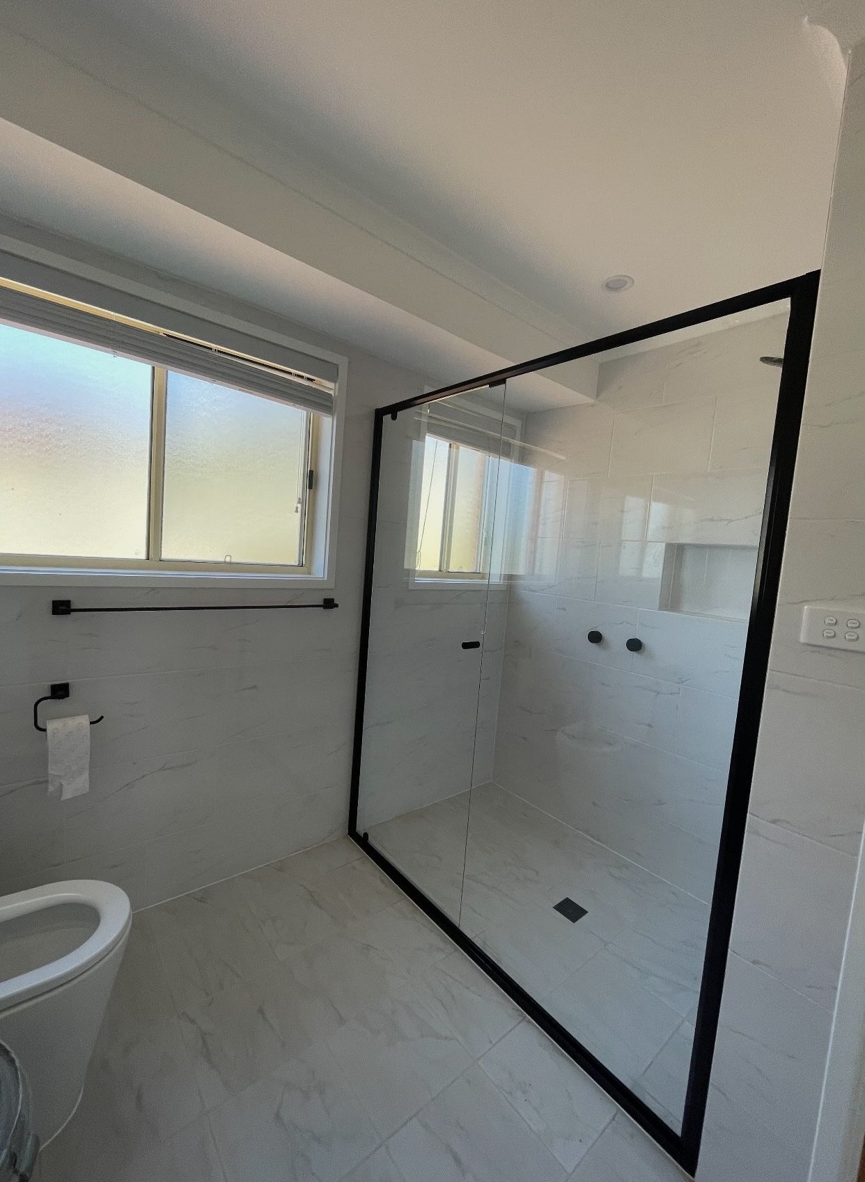 A bathroom with a toilet , shower , and window.