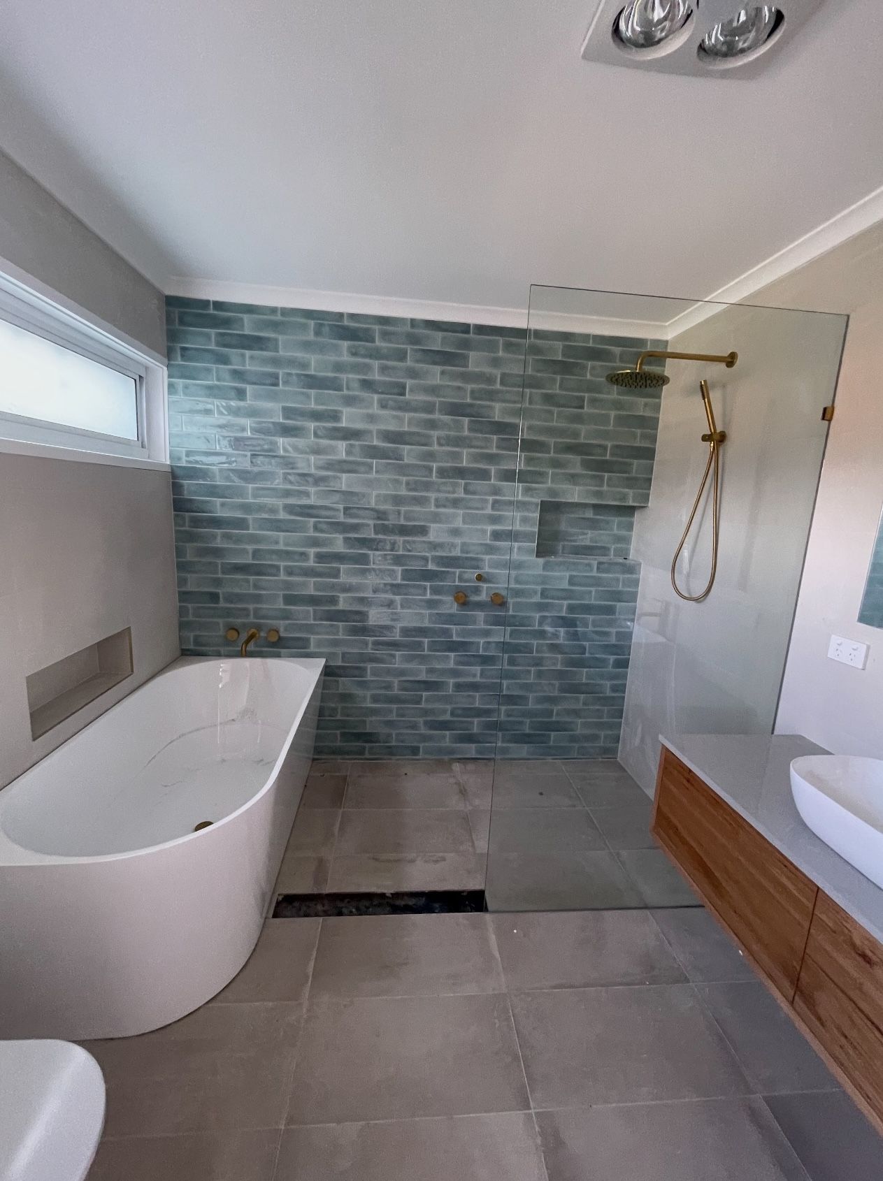 A bathroom with teal tiled walls , a bathtub , sink , toilet and walk in shower.
