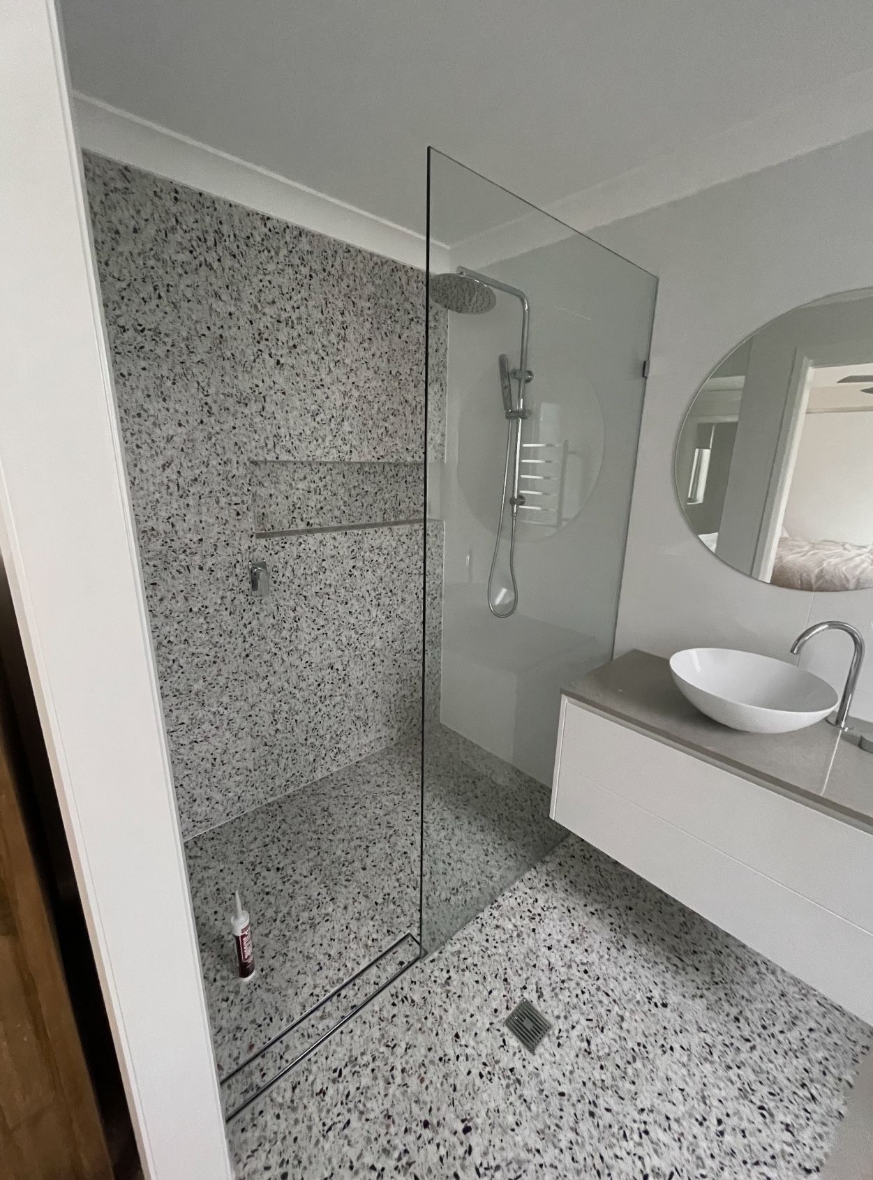 A bathroom with a speckled tile walk in shower , sink and mirror.