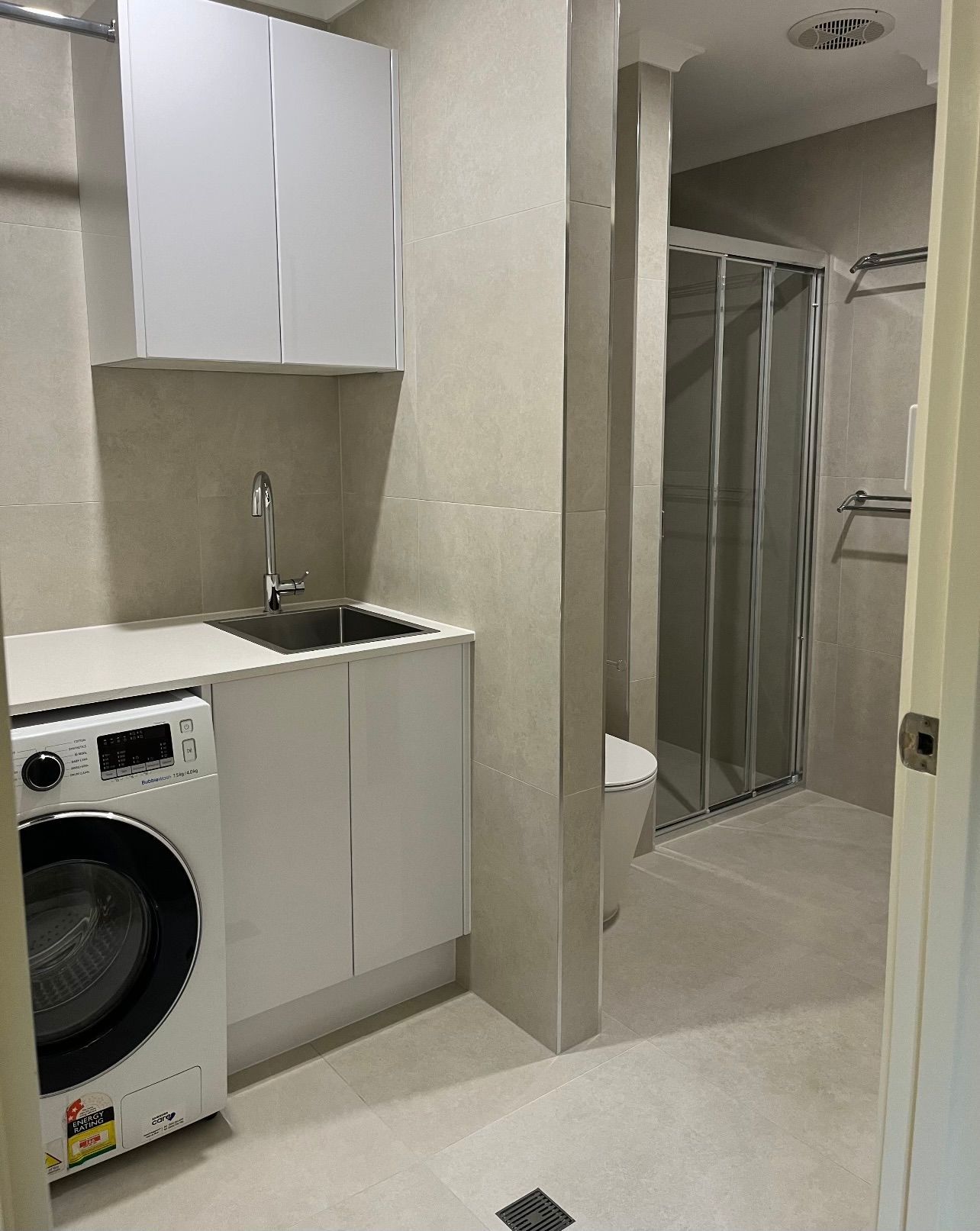 A laundry room with a washing machine , sink , toilet and shower.
