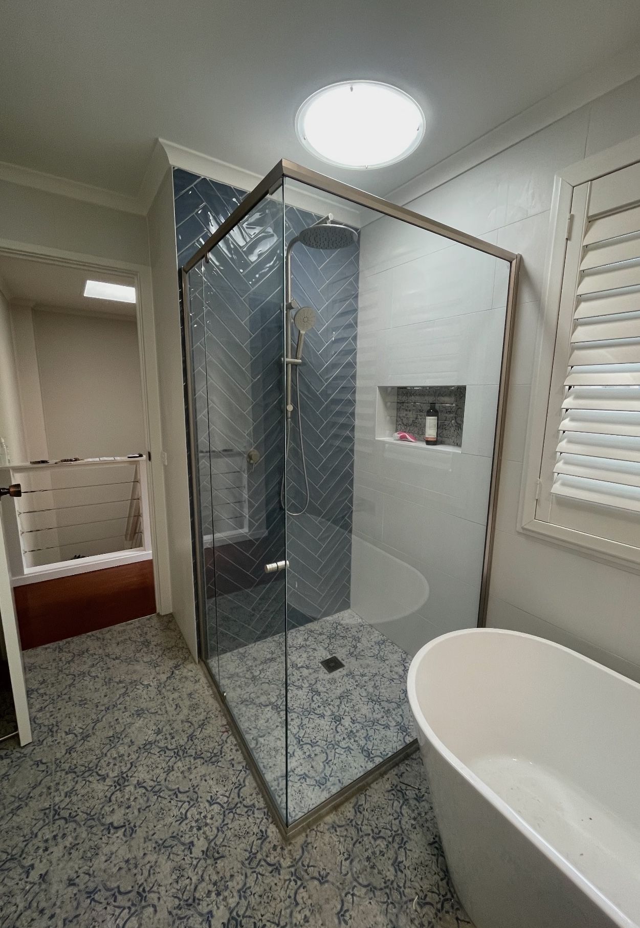A bathroom with a walk in shower with black tiling and a bathtub.