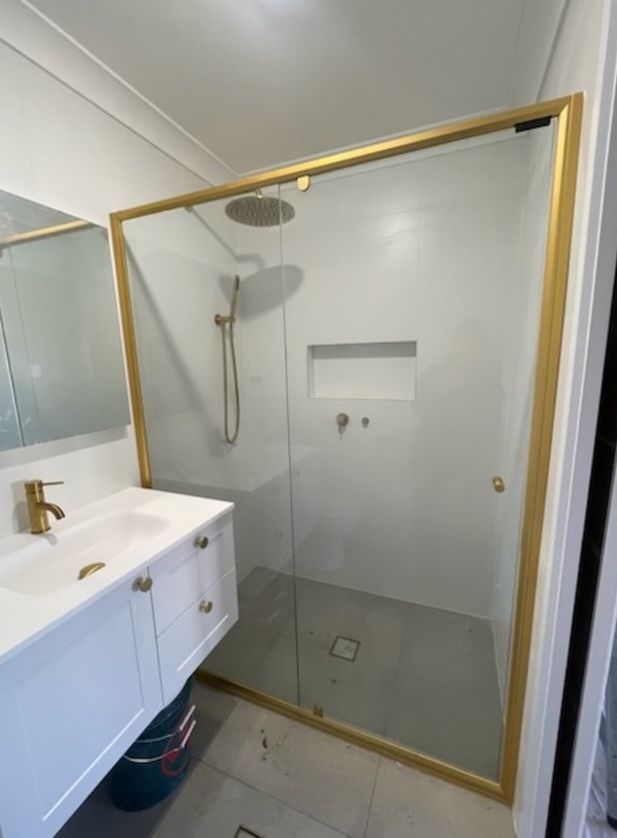 A bathroom with a sink and a shower with a gold frame