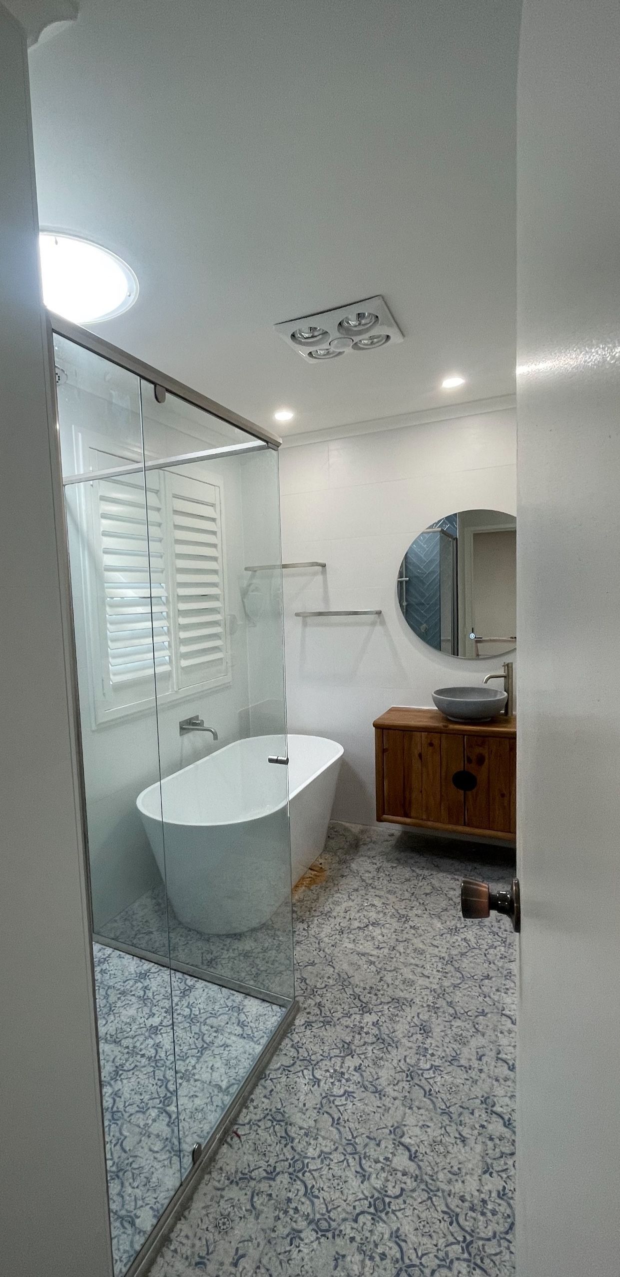 A bathroom with a tub , sink and circle mirror.