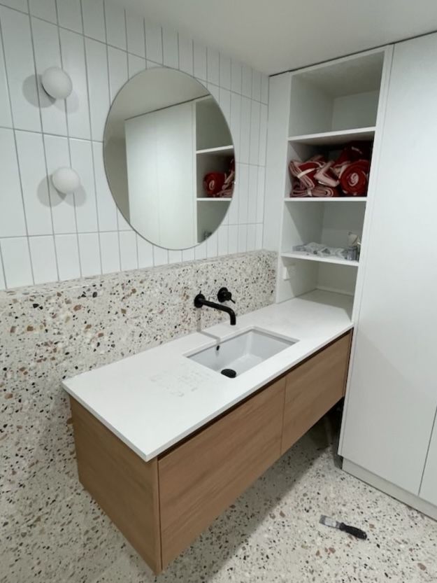 A bathroom with a sink and a round mirror with tiled backsplash