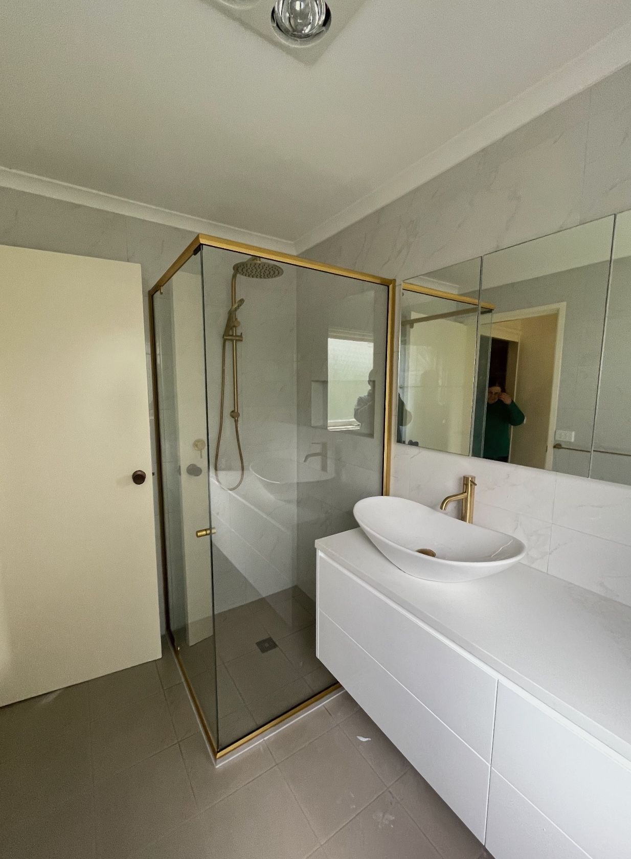 A bathroom with a sink , shower with gold detialing and mirror.
