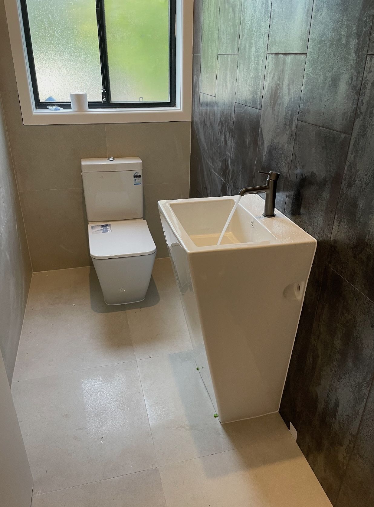 A bathroom with a toilet , sink , dark wall and window.