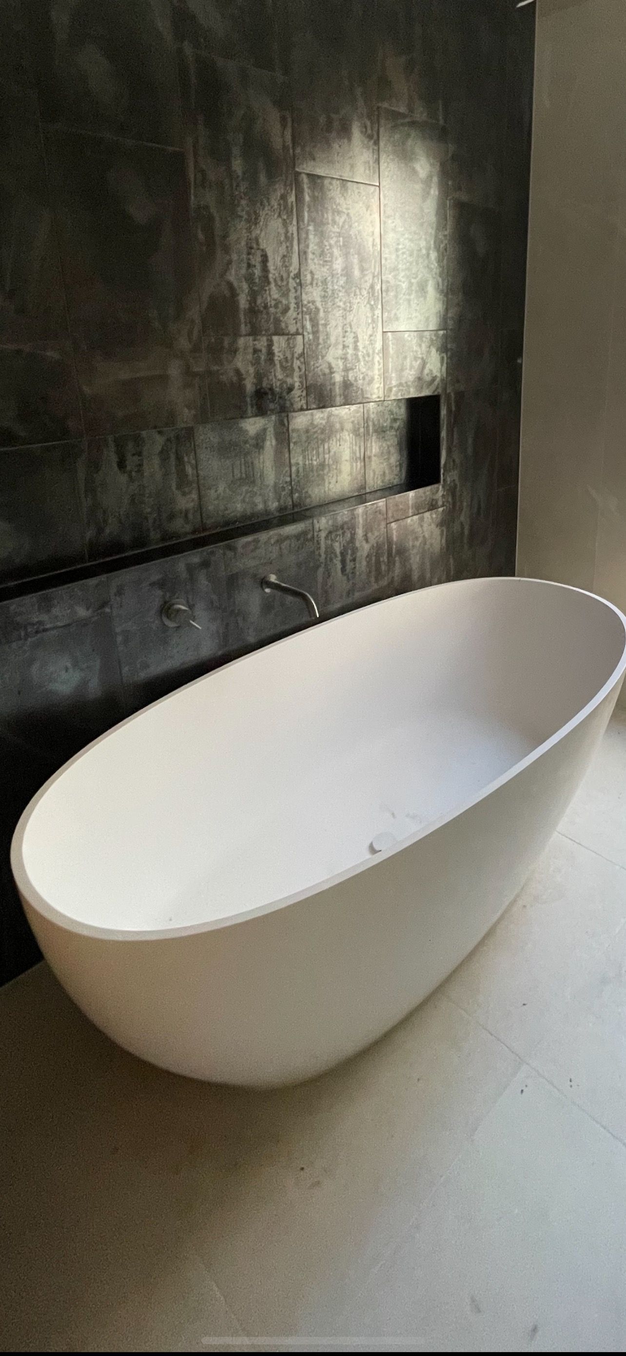 A large white bathtub is sitting in a bathroom next to a black wall.