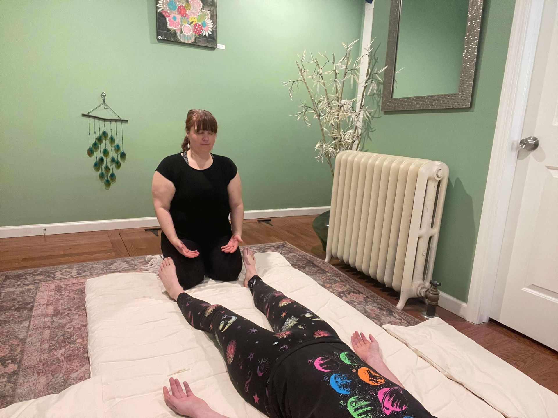 A woman is kneeling down next to a child laying on a mat.