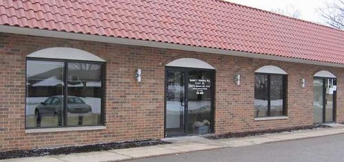 Brick building with arched windows and door, red tile roof, and a car reflected in the window.