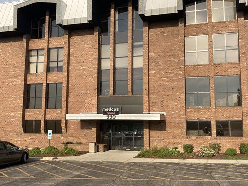 Brick building with windows and a dark entrance under a small awning, fronted by a parking lot and a car.