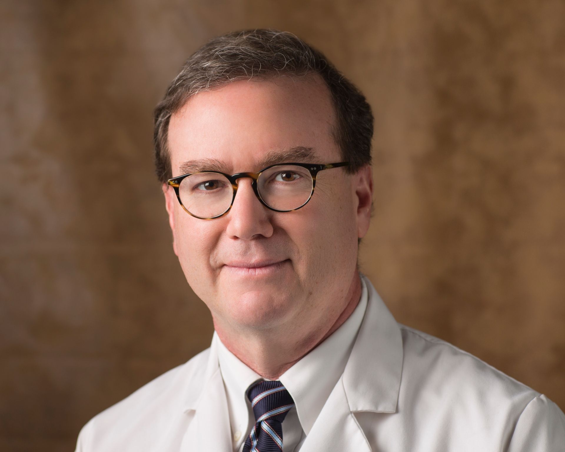 A man wearing glasses and a white coat and tie
