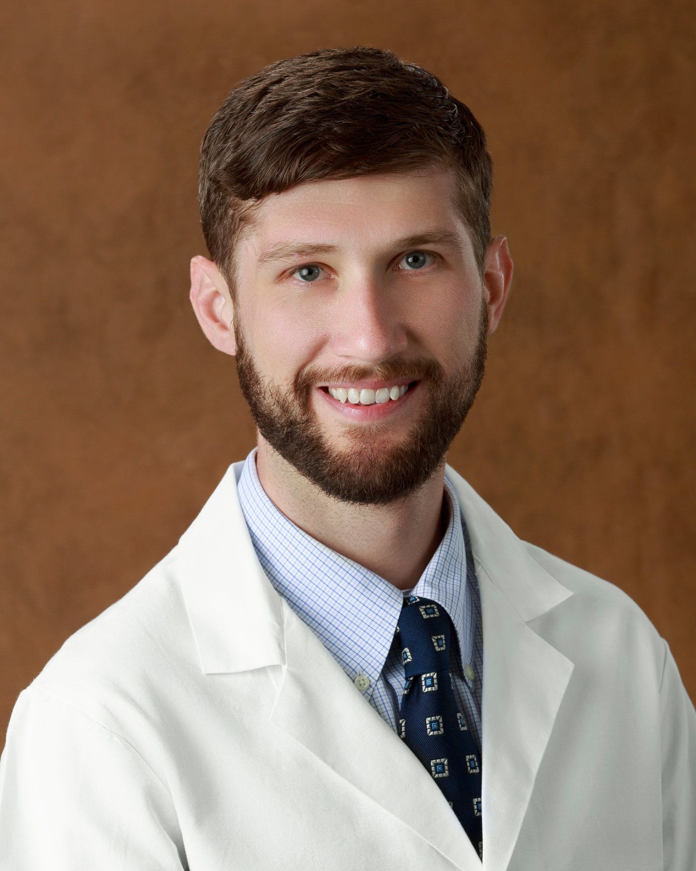 A man with a beard is wearing a white coat and tie.