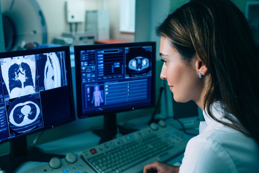 A woman is sitting in front of two computer monitors.