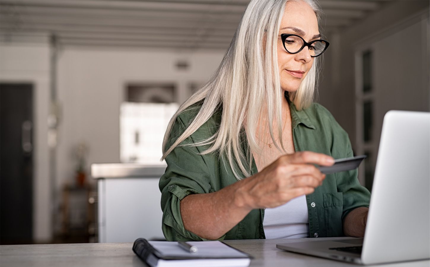 A woman is holding a credit card while using a laptop computer.