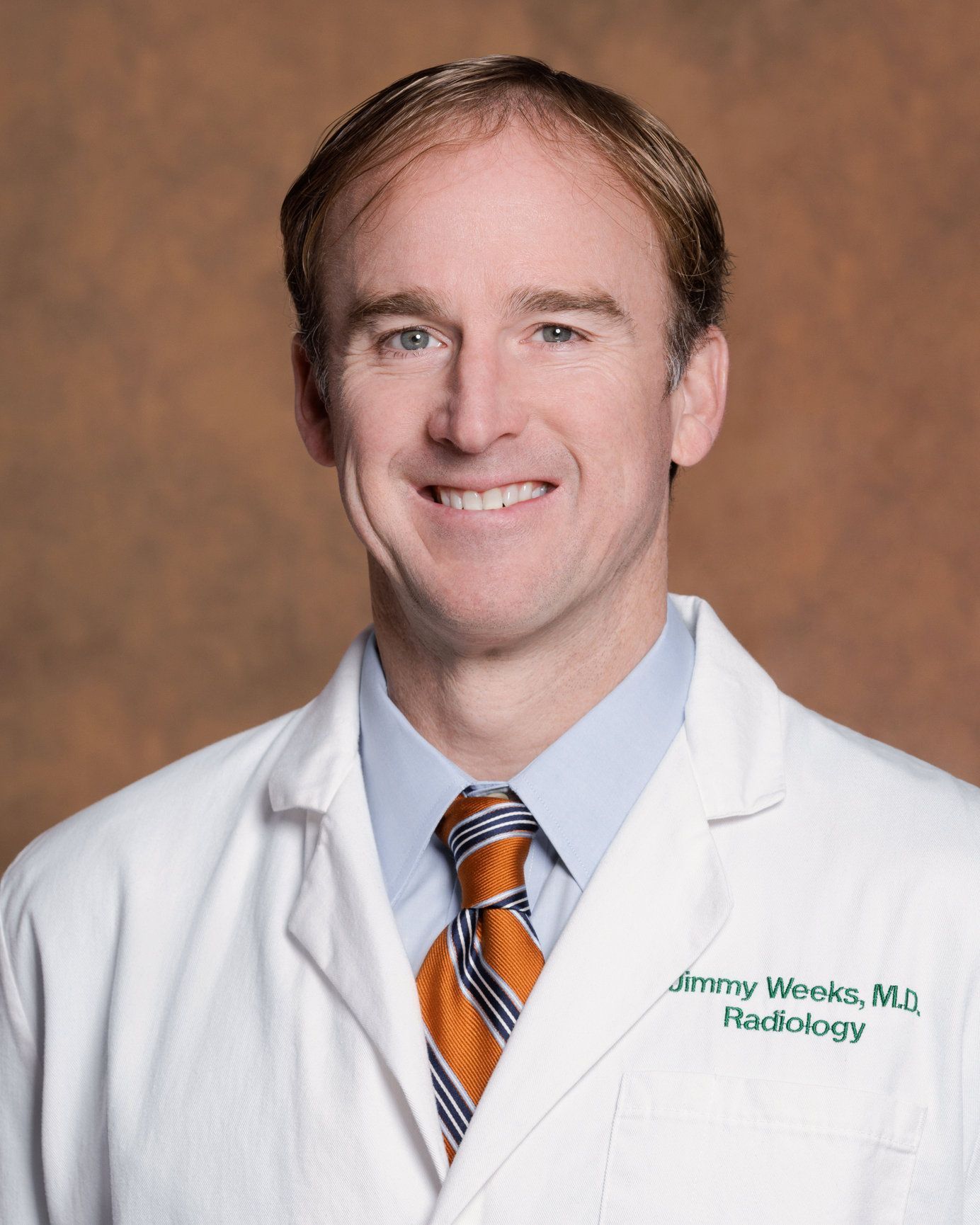 A man wearing a white coat and tie is smiling for the camera