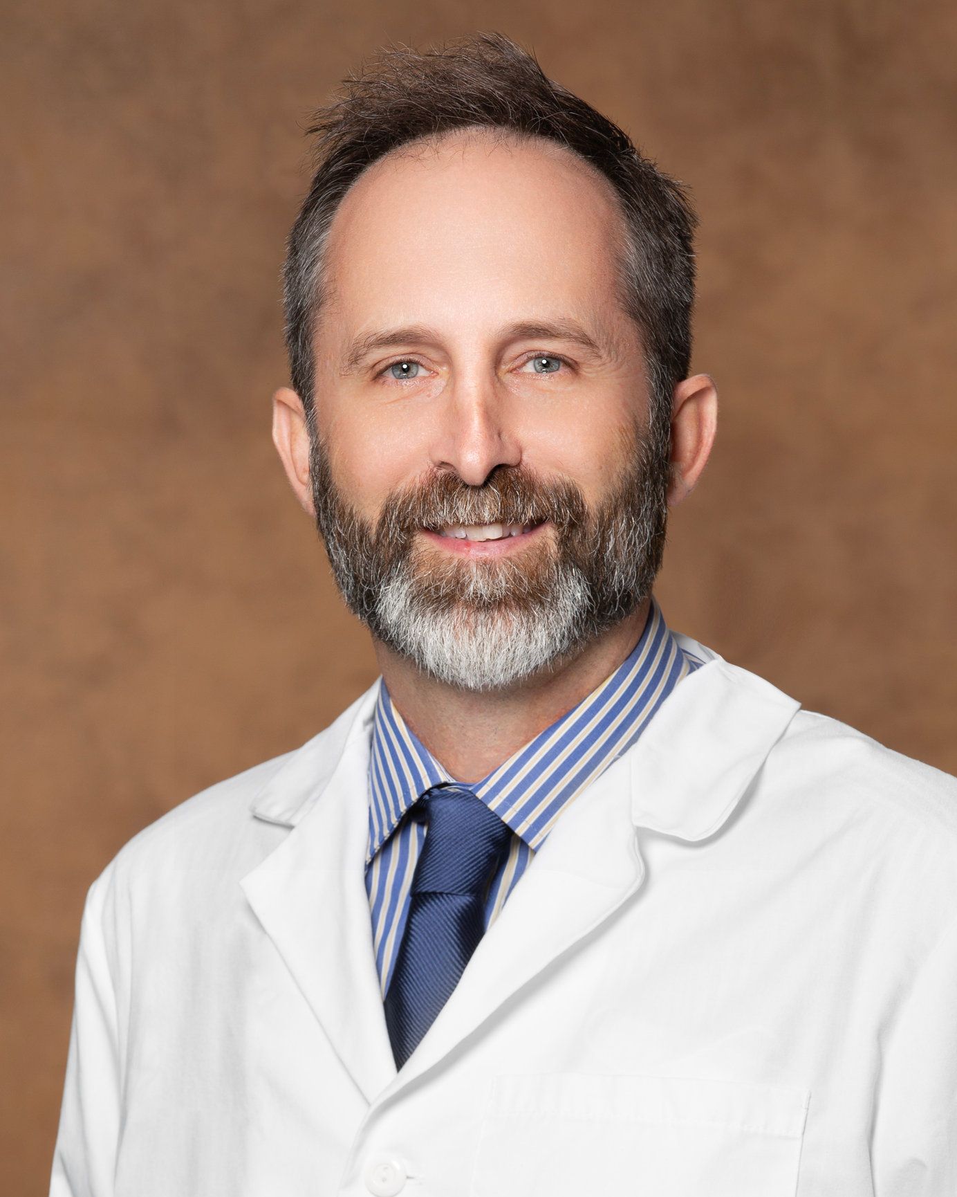 A man with a beard is wearing a white coat and tie.
