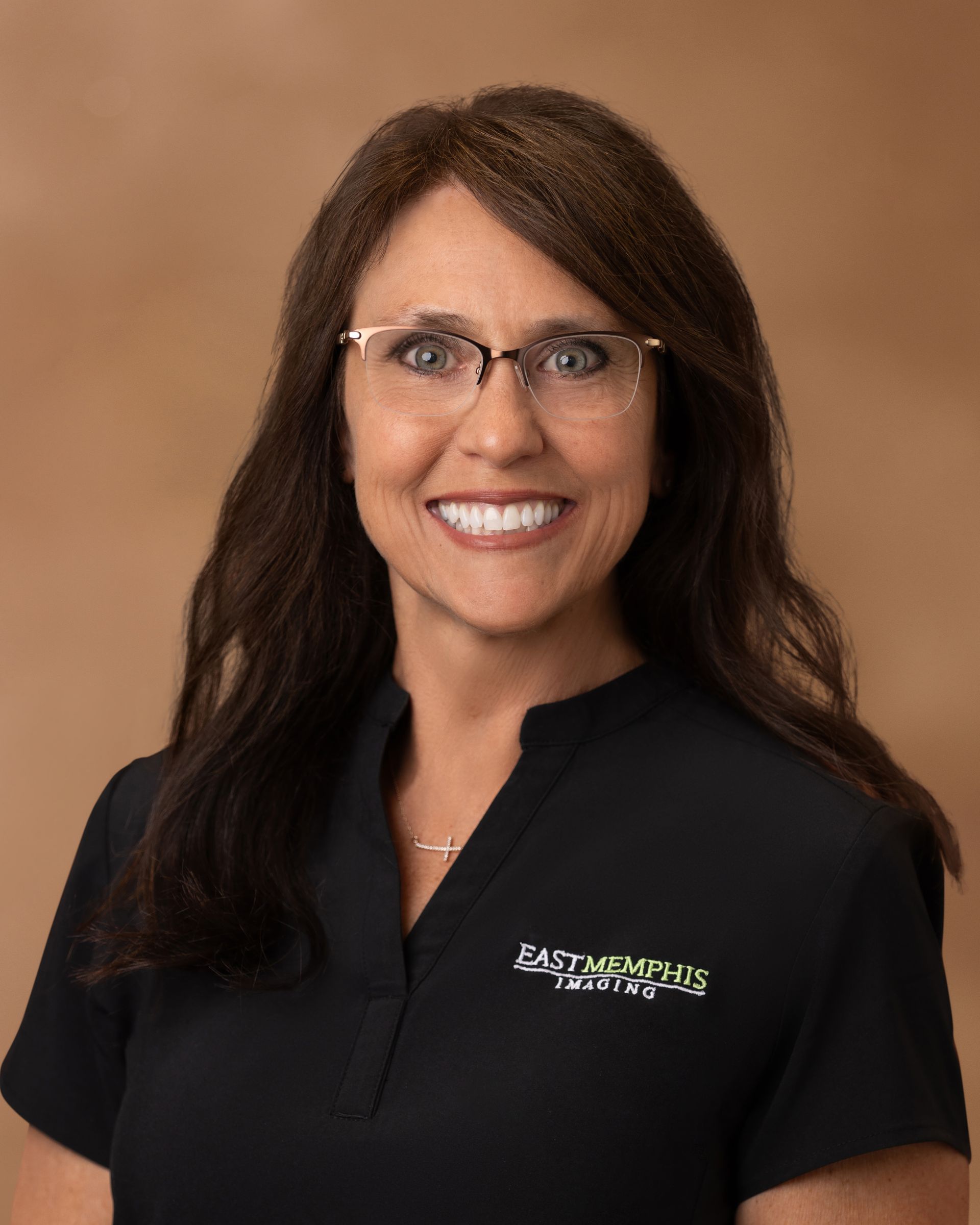 Woman in black polo shirt smiling against a tan studio background