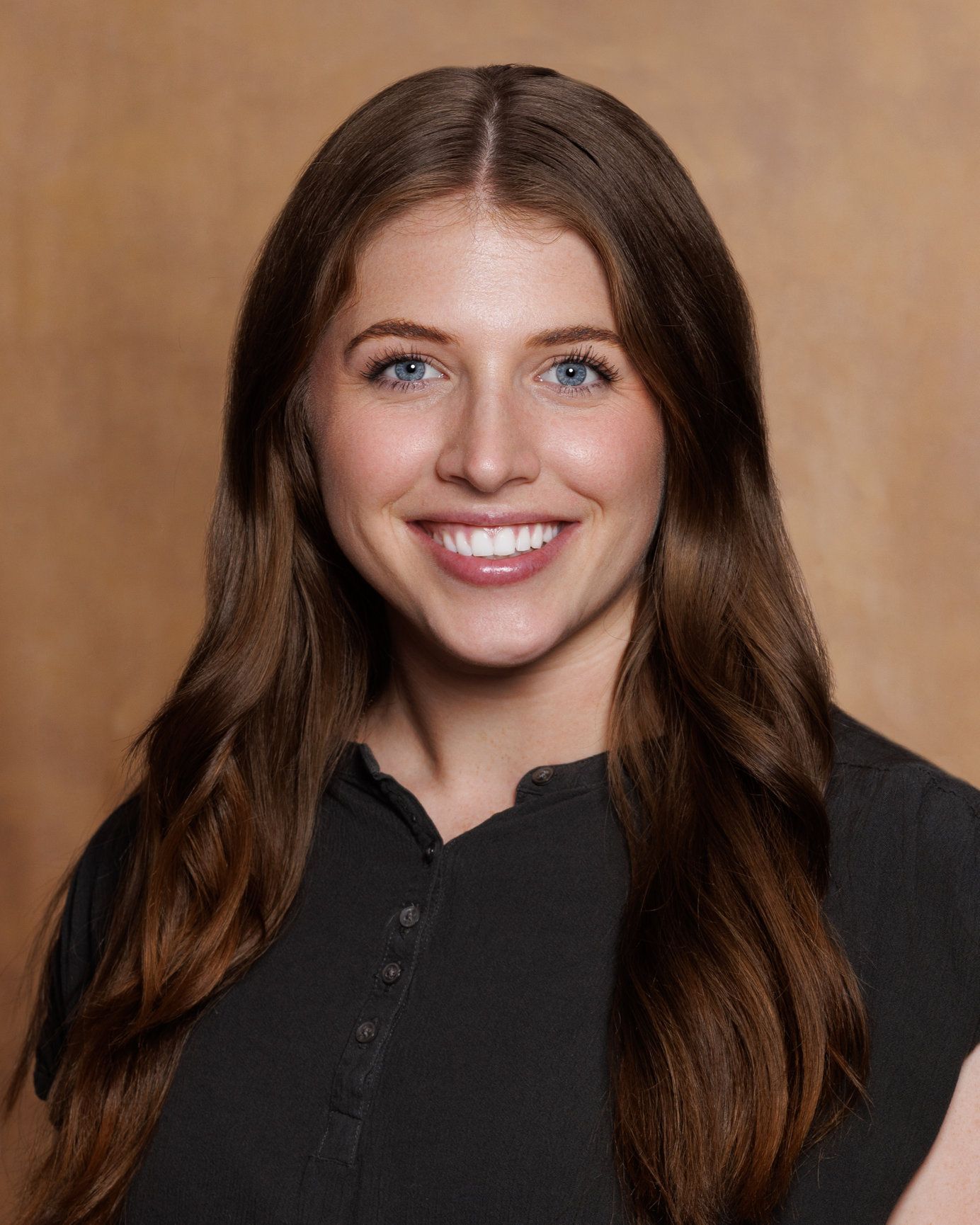 A woman with long brown hair is smiling and wearing a black shirt