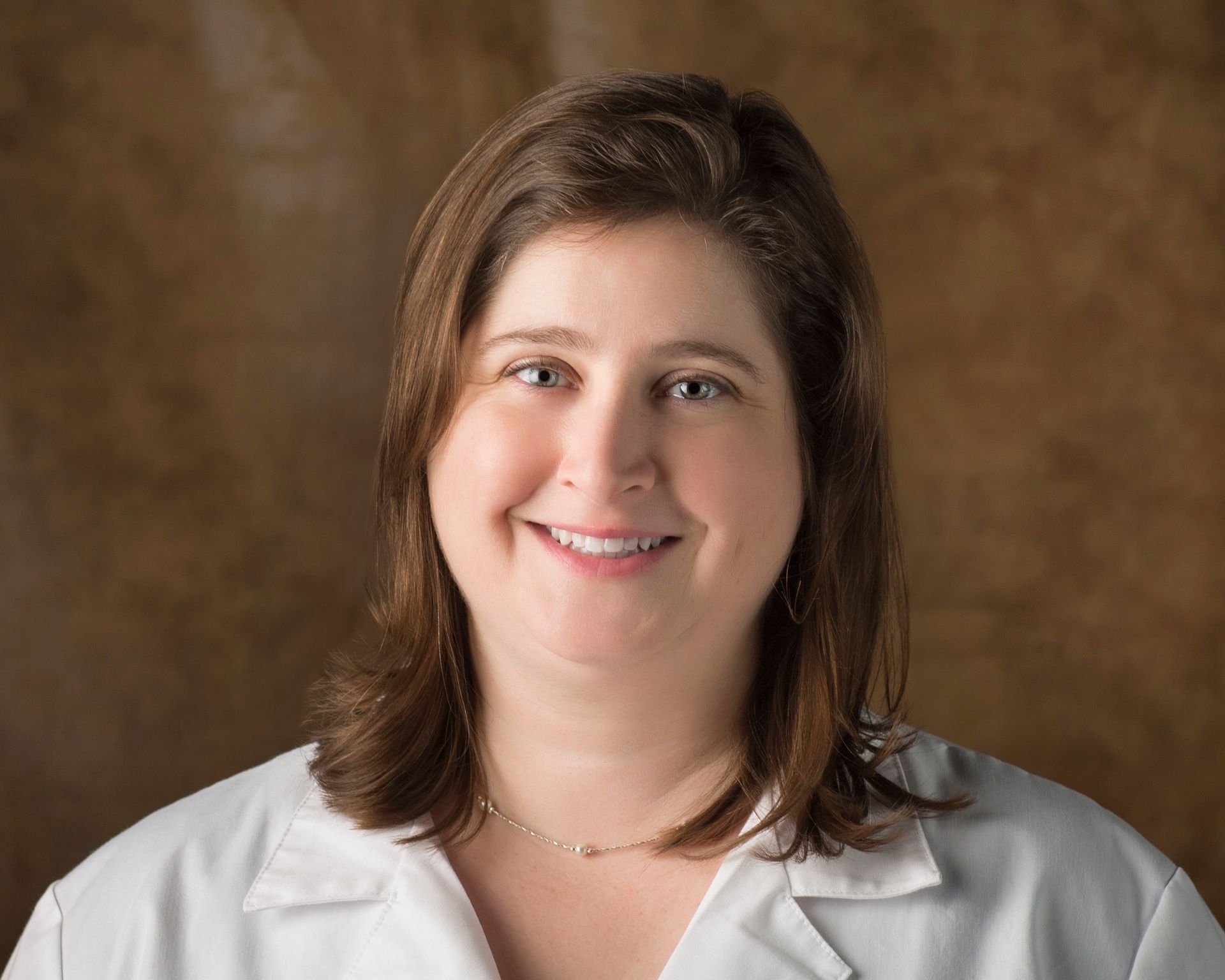 A woman in a white lab coat is smiling for the camera