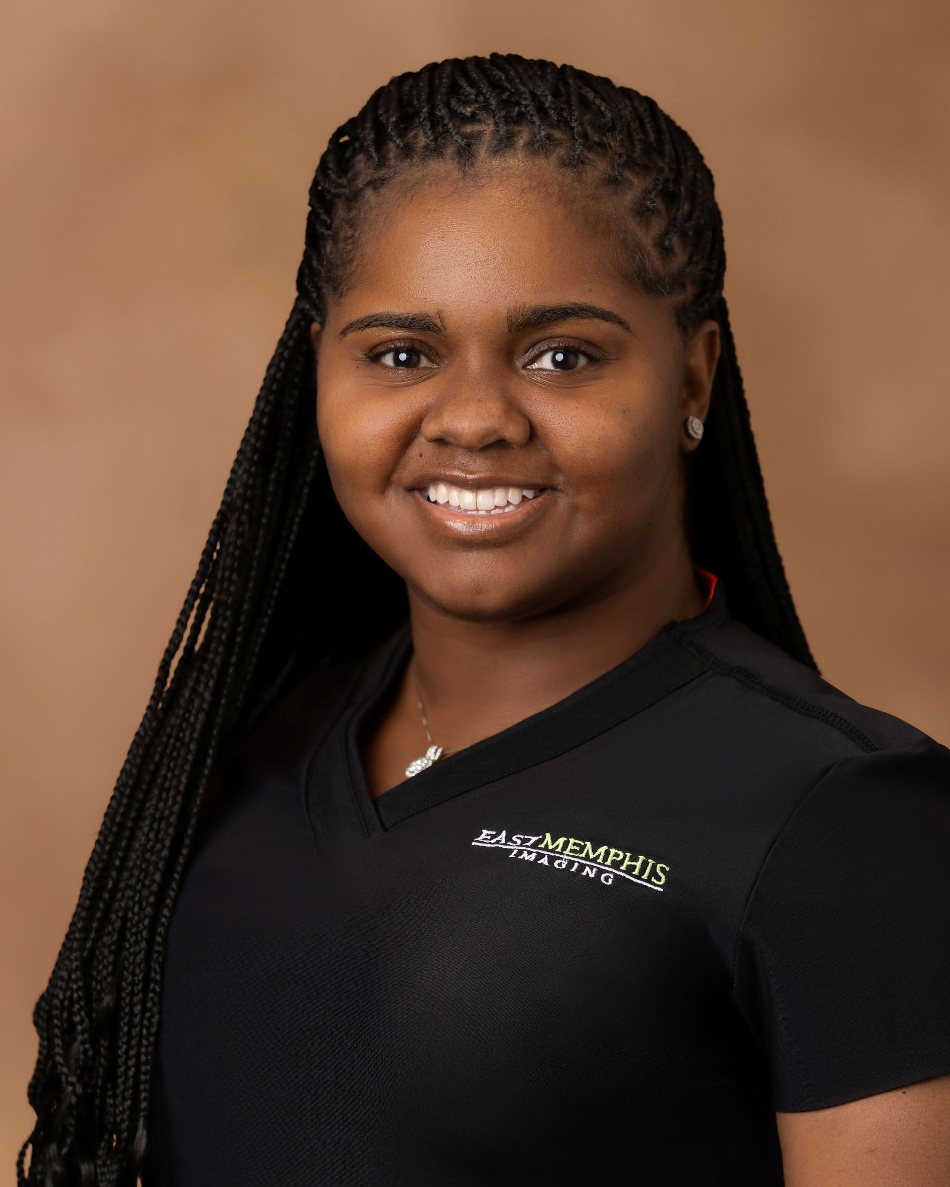 Portrait of a smiling person with long braids wearing a black shirt against a tan background
